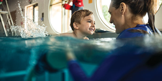 Little boy learning how to swim with instructor
