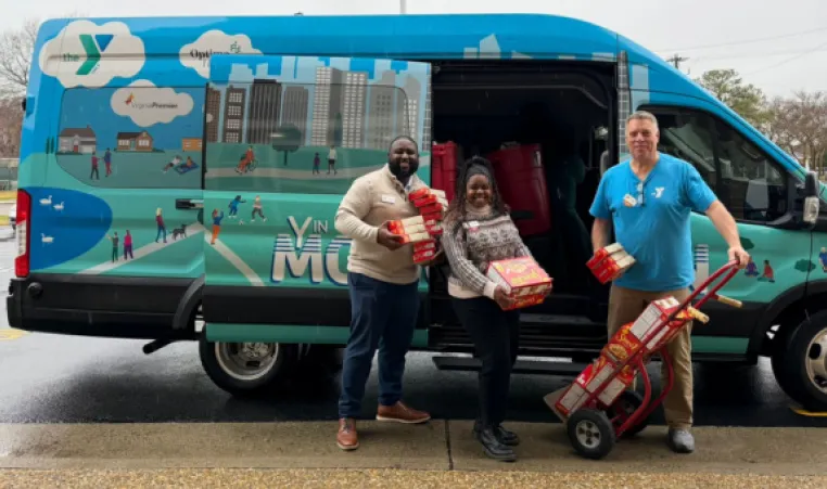 three staff members standing infront of a van with donated food items