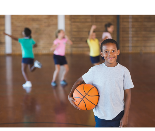 boy with basketball with kids playing in the background